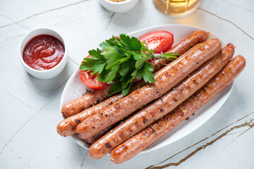 Barbecued sausages with fresh parsley, dips and beer on a light-beige stone background, studio shot