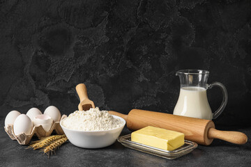 Ingredients for baking and rolling pin on table against black background