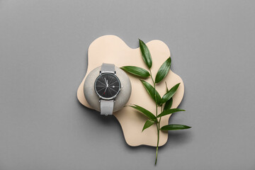 Showcase pedestal with wristwatch and plant branch on grey background