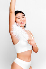Fototapeta premium close up of asian woman with clean skin is using feather touching her hairless white smooth armpit tenderly. Chinese girl holds a white feather concept of laser hair removal, depilation hair removal