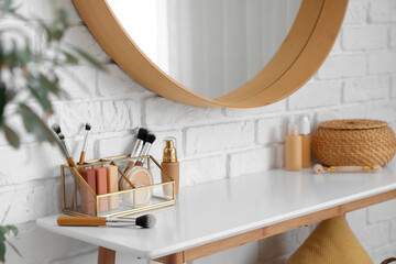 Organizer with makeup brushes and decorative cosmetics on table near white brick wall