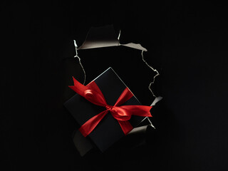 Black Friday sale. Holiday present. Night shopping. Gift box with red ribbon in breakthrough paper...