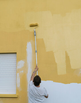 Rear view of a man painting a house yellow with a paint roller, Spain