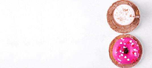 Fototapeta premium Web banner with donut with pink icing and heart shaped sprinkles and cup of cappuccino on white table. Mockup with copy space