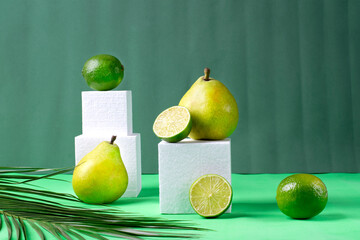 Pears and limes on white cube podiums against green background with palm leaves. Creative geometric...