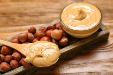Spoon with tasty hazelnut butter on wooden table, closeup