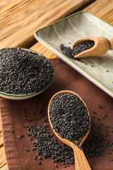 Spoon and bowl of black sesame seeds on wooden table, closeup