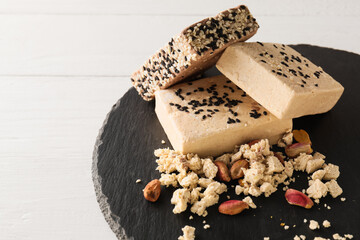 Slate board of tasty sesame halva with pistachios on light wooden background, closeup