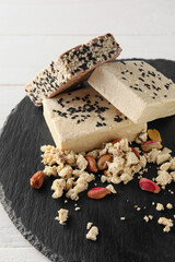 Slate board of tasty sesame halva with pistachios on light wooden background, closeup