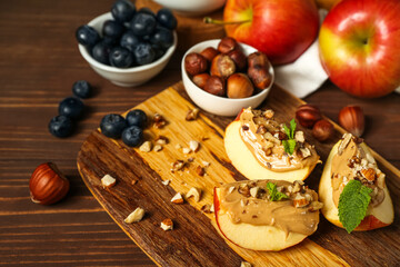 Board of tasty apple wedges with nut butter, hazelnuts and blueberry on wooden background, closeup