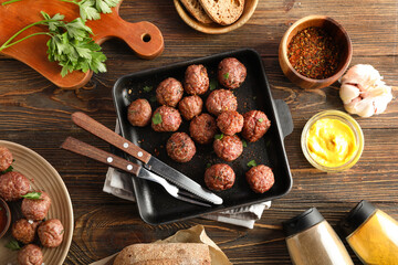 Baking dish with meat balls, cutlery, sauce and spices on wooden background