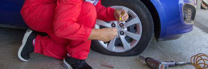 Tire specialist in his workshop while he repairs a punctured wheel of a car with patch and putty. Do it yourself work. Horizontal banner 
