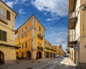Fossano, Piedmont, Italy - September 09, 2022: View of Via Roma cobblestone street with ancient buildings and arcades and the civic tower in the background