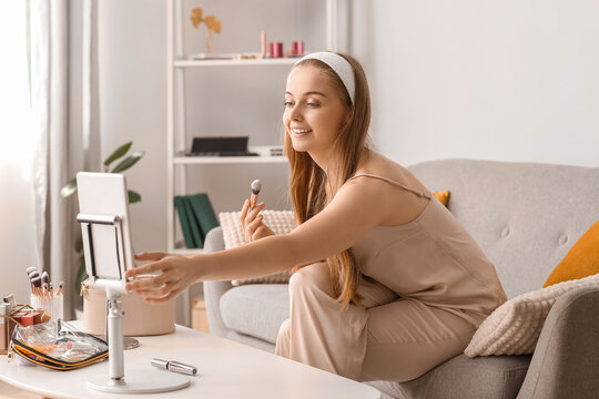 Female beauty blogger with makeup brush recording video at home