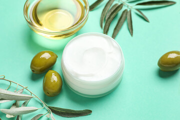 Jar of cream with green olives, plant branches and oil on color background, closeup