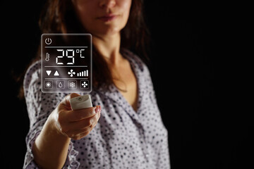 A woman in pajamas sets the temperature in the heating and air conditioning system of a bedroom,...