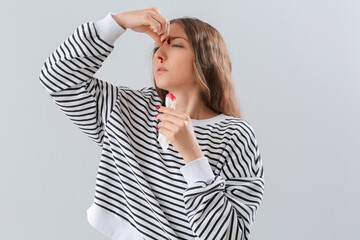 Young woman with nosebleed and tissue on light background
