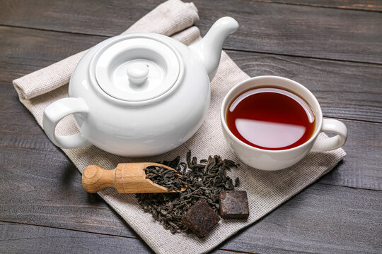 Napkin with scoop of dry puer tea, cup and teapot on dark wooden background
