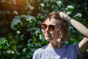 Attractive woman in sunglasses enjoying flowering of apple trees walking in spring garden. Happy female portrait.