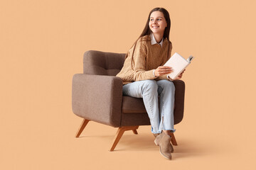 Fototapeta na wymiar Beautiful woman reading book in armchair on beige background