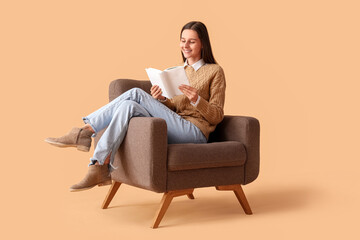 Fototapeta na wymiar Beautiful woman reading book in armchair on beige background