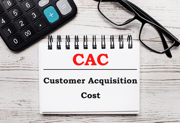 On a light wooden table calculator, glasses and a blank notepad with the text CAC Customer Acquisition Cost. Business concept