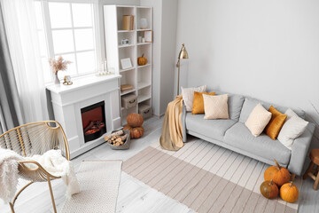 Autumn interior of living room with grey sofa, fireplace and pumpkins