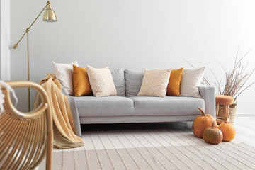 Fototapeta na wymiar Autumn interior of living room with grey sofa, lamp and pumpkins