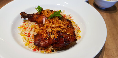 Grilled chicken with Basmati rice and topping with fried onion and garlic on white dish. Close up Islamic food in plate on brown wooden table.   
