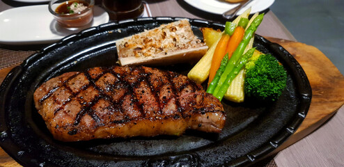 Australian beef steak with carrot, corn, broccoli and potato on black hot pan. Meat grilled or barbecue with fresh vegetable at restaurant. Big meal at lunch time