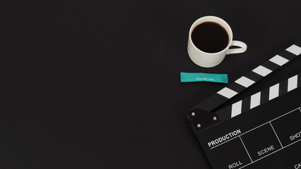 Black Clapper board and hot coffee white cup and blue sugar sachet  on black background.