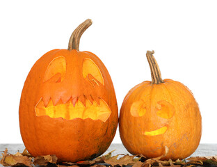 Carved Halloween pumpkins with fallen leaves on table against white background