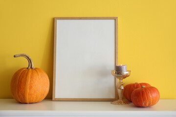 Blank frame with Halloween pumpkins and candle on mantelpiece near yellow wall