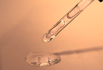 Glass dropper with a liquid transparent beauty product on a plain beige background close-up. Cosmetic care product.