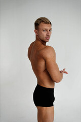 Obraz premium muscular male bodybuilder in black shorts on a white background, a muscular back in a young man.