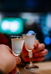 Two hands clinking shots of alcoholic beverage in bar