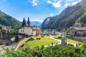 Fototapeta premium Lillianes, Aosta Valley. Italy. View of the stone bridge over the Lys stream, the Church of San Rocco and the cemetery. July 27, 2022.