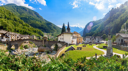Fototapeta na wymiar Lillianes, Aosta Valley. Italy. View of the stone bridge over the Lys stream, the Church of San Rocco and the cemetery. July 27, 2022.