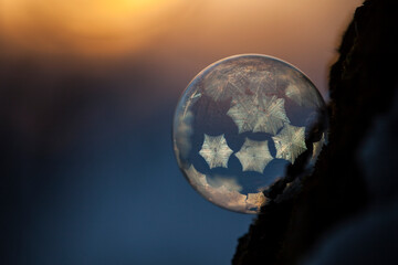 Close-up of frozen bubble against sky during sunset in orange blue light with small crystals