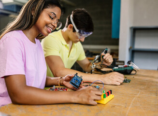 Young diverse students learning together at stem robotics class - Hispanic latin female building...