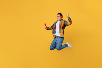 Fototapeta na wymiar Full body young fun happy cool middle eastern man wears casual shirt white t-shirt headphones listen music jump high do winner gesture hold use mobile cell phone isolated on plain yellow background.