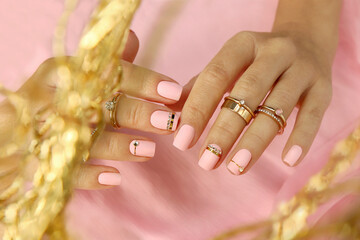 Manicure on short nails with white pink nail polish with golden rings on the fingers.