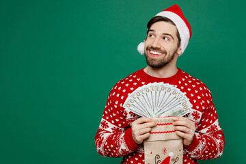 Merry fun young man wear red knitted sweater Santa hat posing hold stocking sock fan of cash money...