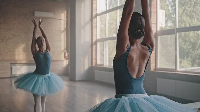 Graceful ballerina dances against large mirror in studio