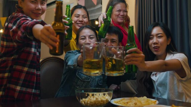 Group of multiethnic adult Asia people use phone greeting friend on remote video call and having hangout party at dining table in night life indoor home. Happy hour millennial generation inside house.