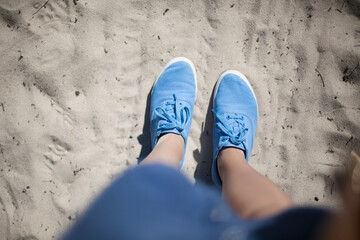 Women's feet in blue sneakers on white sand. white sand underfoot