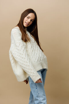 An Elegant Woman Stands On A Light Background In A White Sweater Posing Taking A Small Step Forward, Waving Her Arms A Little To The Sides And Hiding Them Behind Her Back