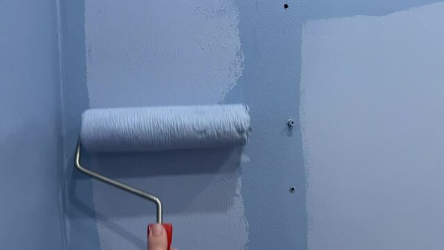 A man's hand holds a roller brush and paints the wall in lilac color