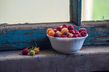 Raspberries in a white cup. On a wooden background with green leaves. A vase of red and white raspberries on boards.