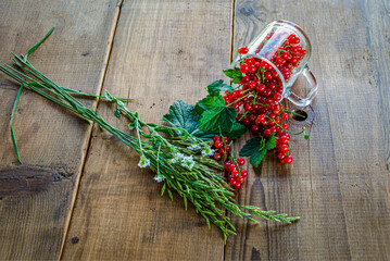 Red currants in a glass. On a wooden background, a light green napkin with leaves and red berries, on a napkin a glass transparent glass with red currant berries. High quality photo